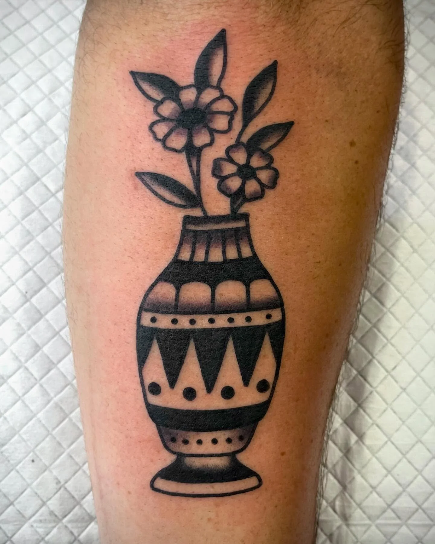Black line tattoo of a decorative vase with flowers on a person's arm.