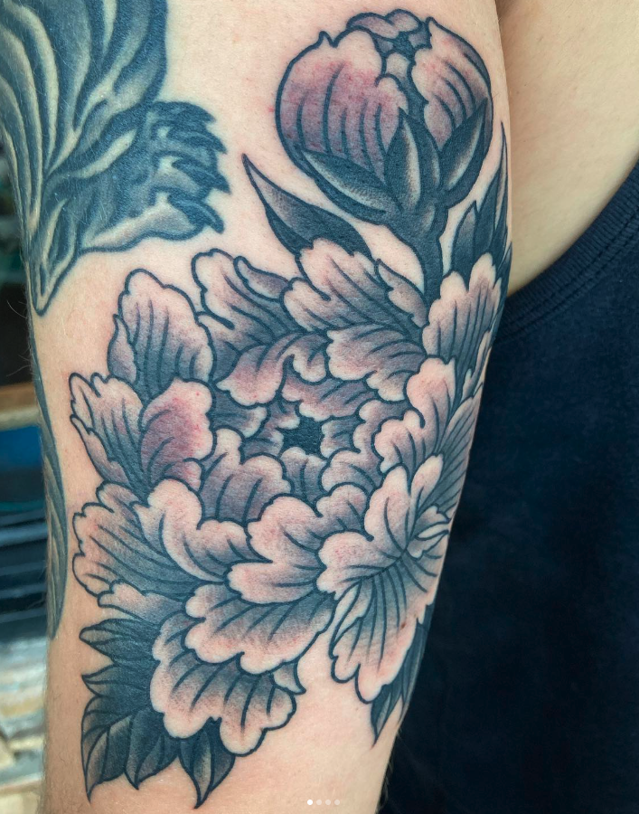 Black and gray tattoo of a peony flower on a person's upper arm.