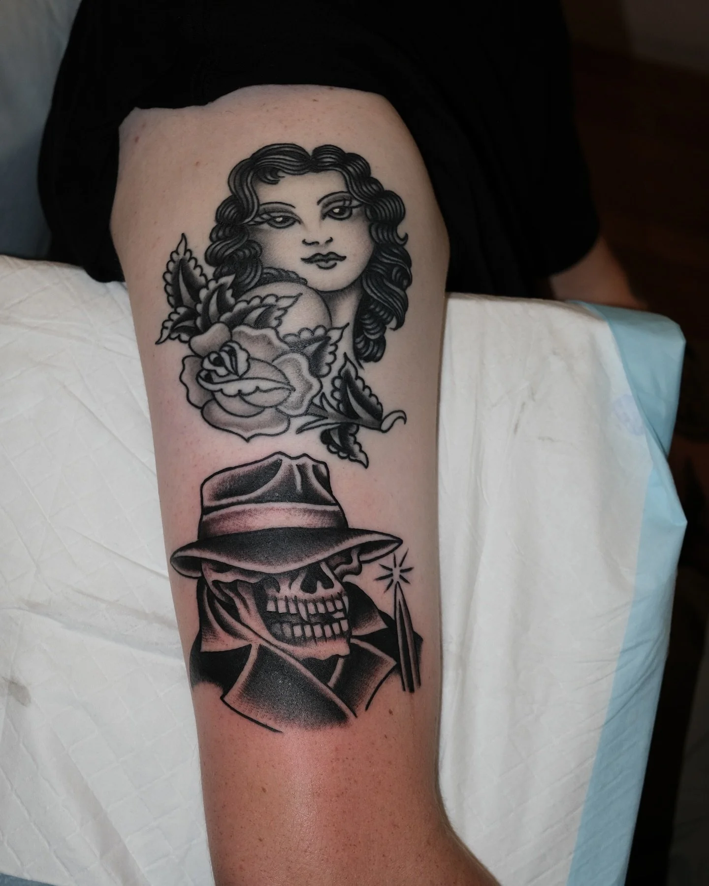 Tattoo of a woman's face with long wavy hair, a rose, a butterfly, and a skeleton wearing a hat with a smoking pipe.