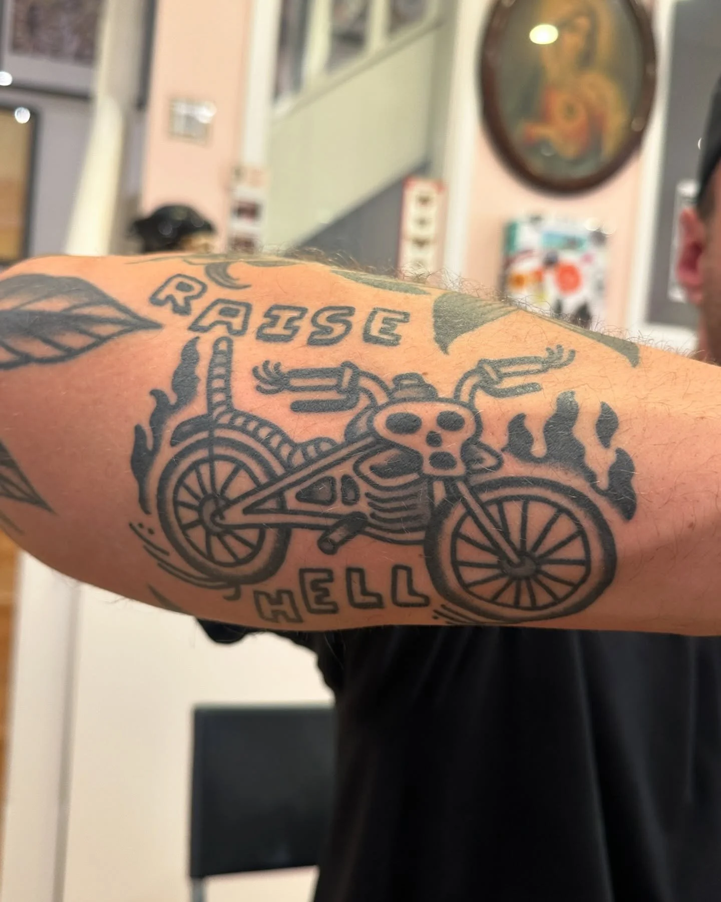 Tattoo on person's arm featuring a skull riding a bicycle with the words "Risse" and "Hell".