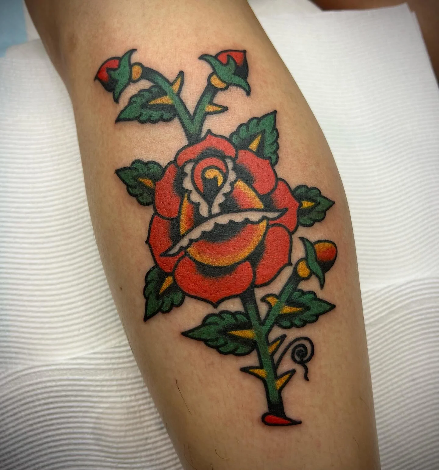 Tattoo of a rose with a swallow inside the bloom, green leaves, and a green stem.
