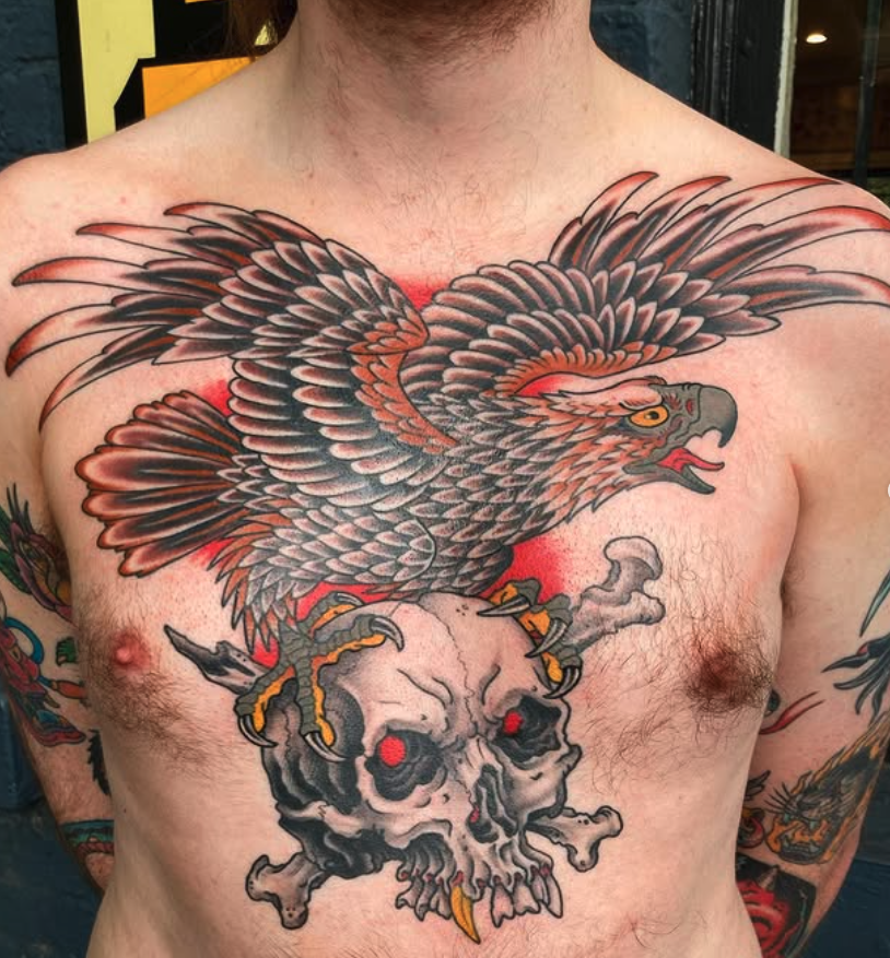 Tattoo of a eagle with extended wings standing on a human skull on a man's chest.