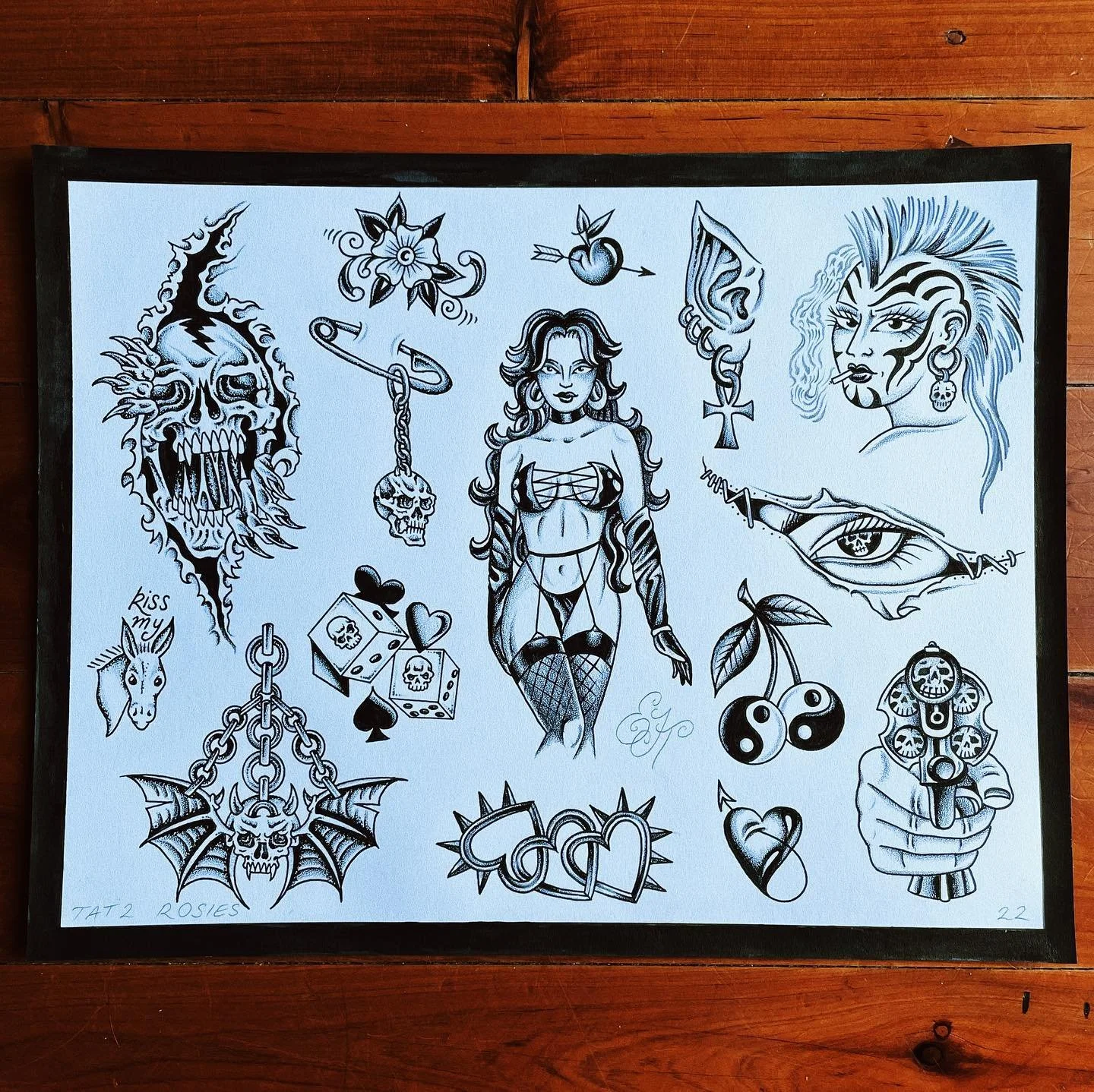 Collection of black and white tattoo-style illustrations including a flaming skull, a woman with long hair and tattoos, a punk woman with shaved side hairstyle, a eye with detailed eyelashes, a hand holding a gun, a pair of cherries, a skull with bat