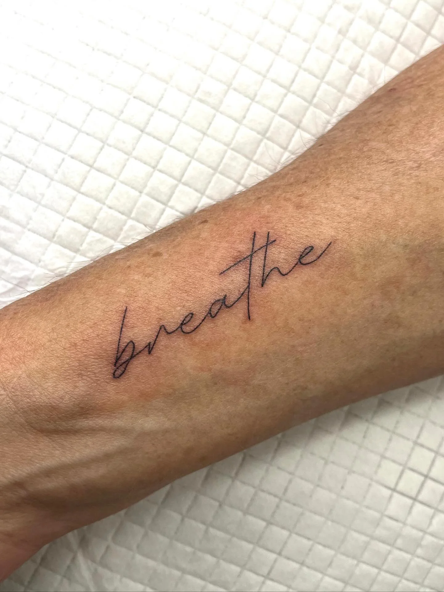 A tattoo on a person's forearm with the words 'breathe' written in cursive script.