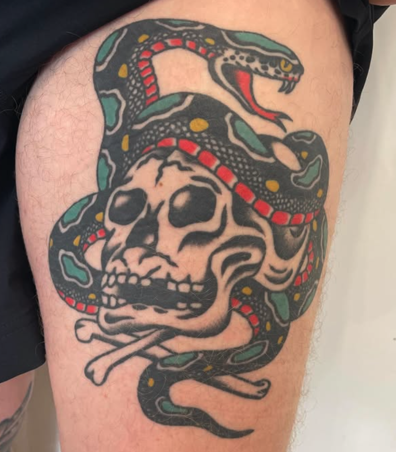 Tattoo of a human skull with a snake wrapped around it, the snake has a yellow pattern and red tongue, and the skull is holding a small bone.