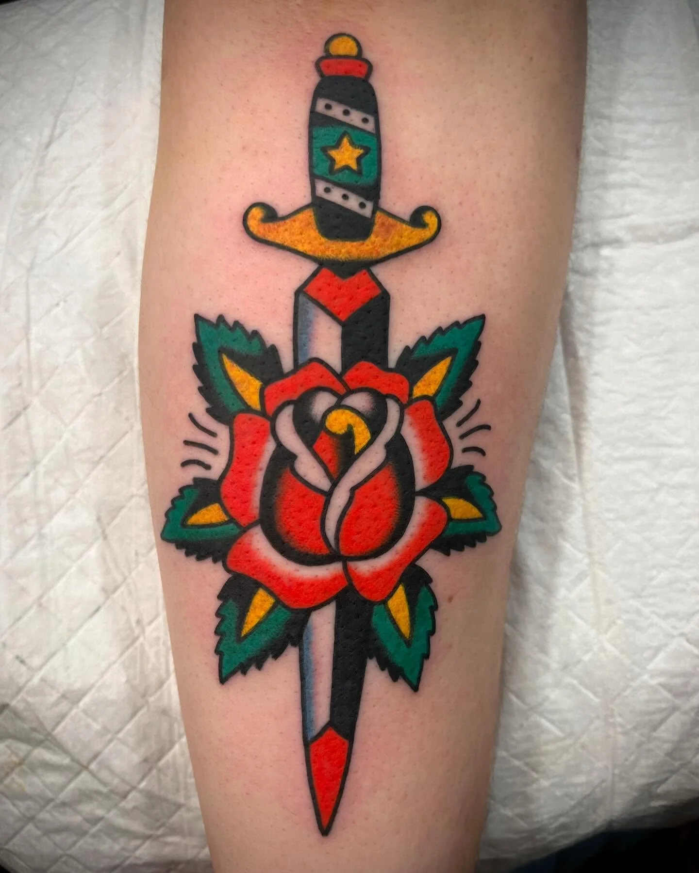 Tattoo of a traditional-style dagger with a rose and leaves.