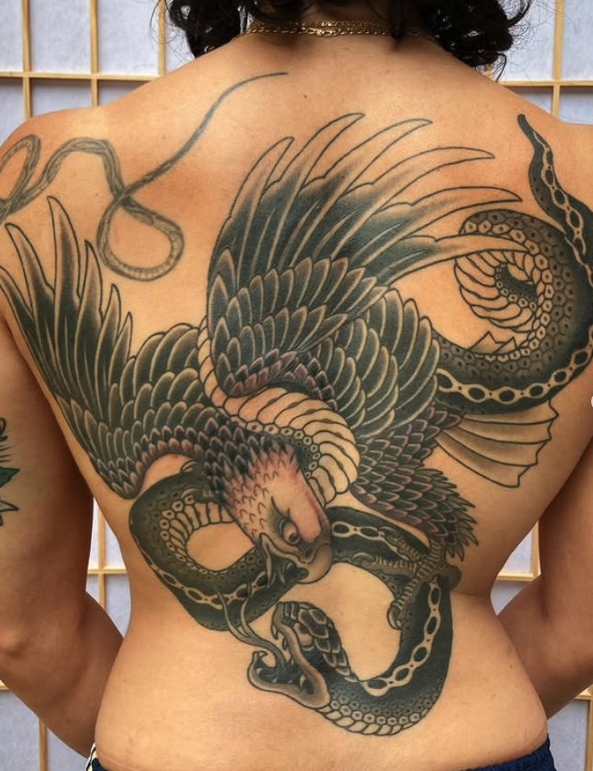 A large tattoo of a snake and a bird covering the person's back. The snake has a detailed pattern and is intertwined with the bird's wings and body, creating an intricate design.