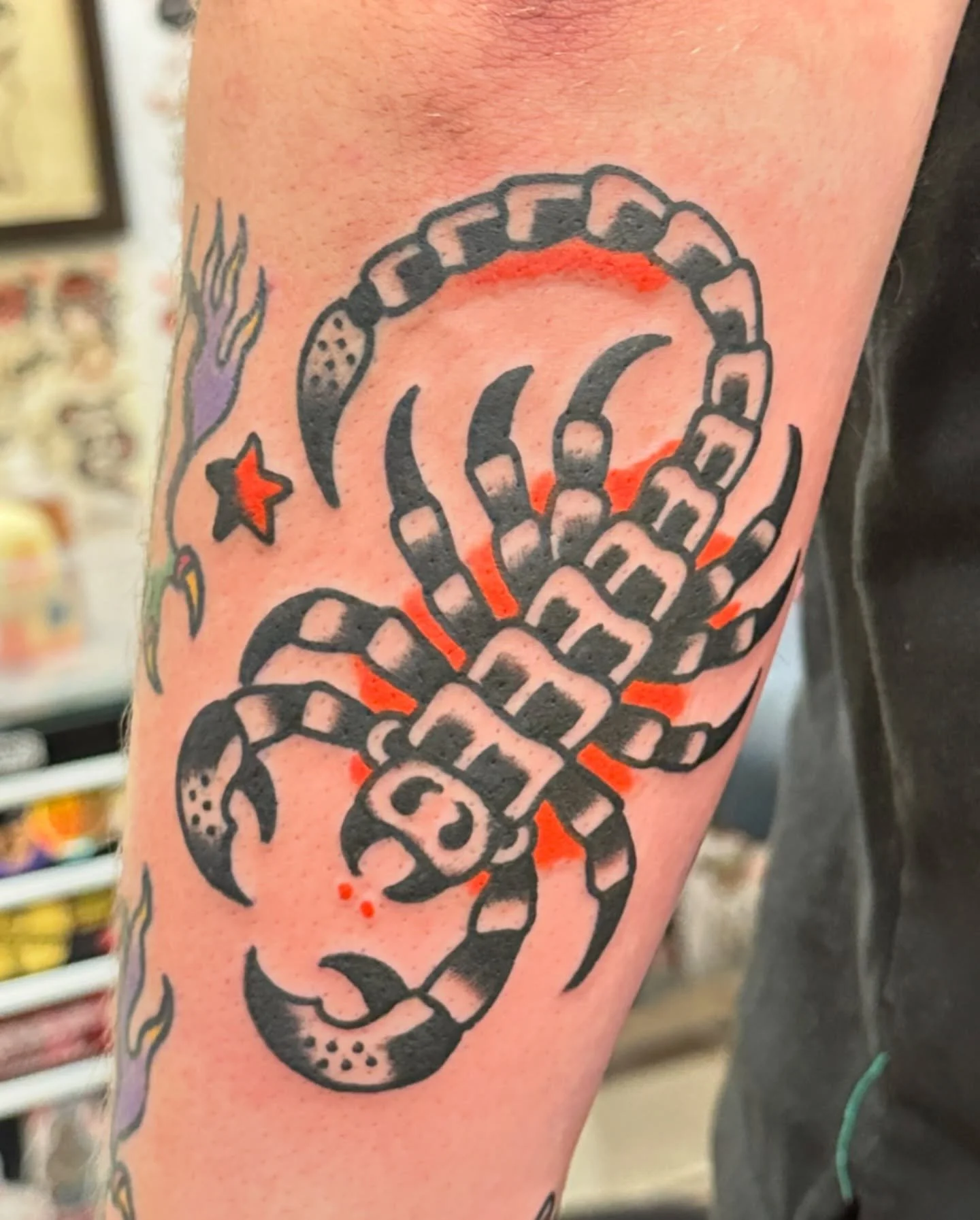 Traditional black and red tattoo of a scorpion on a person's arm.
