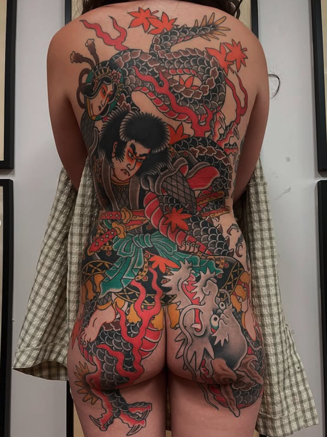 A person with a large Japanese-style tattoo covering their back and bum, depicting a samurai warrior, a dragon, and various traditional Japanese motifs in bold colors.
