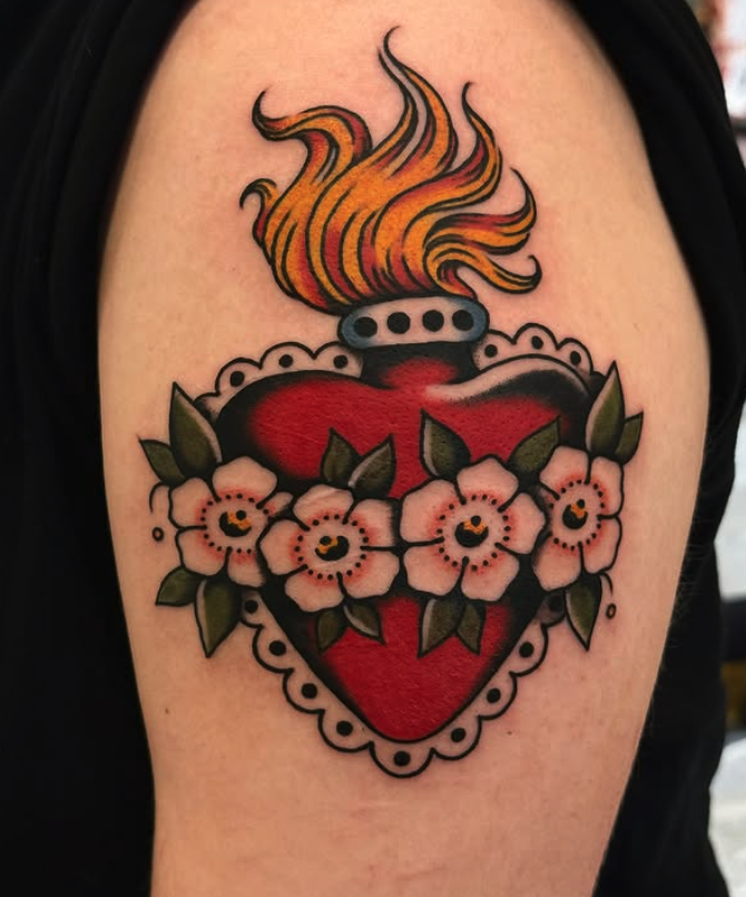 A colorful tattoo of a heart with a fiery flame at the top, surrounded by pink flowers and green leaves.