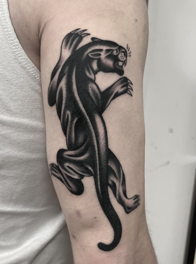 Black and gray tattoo of a roaring panther on person's upper arm.