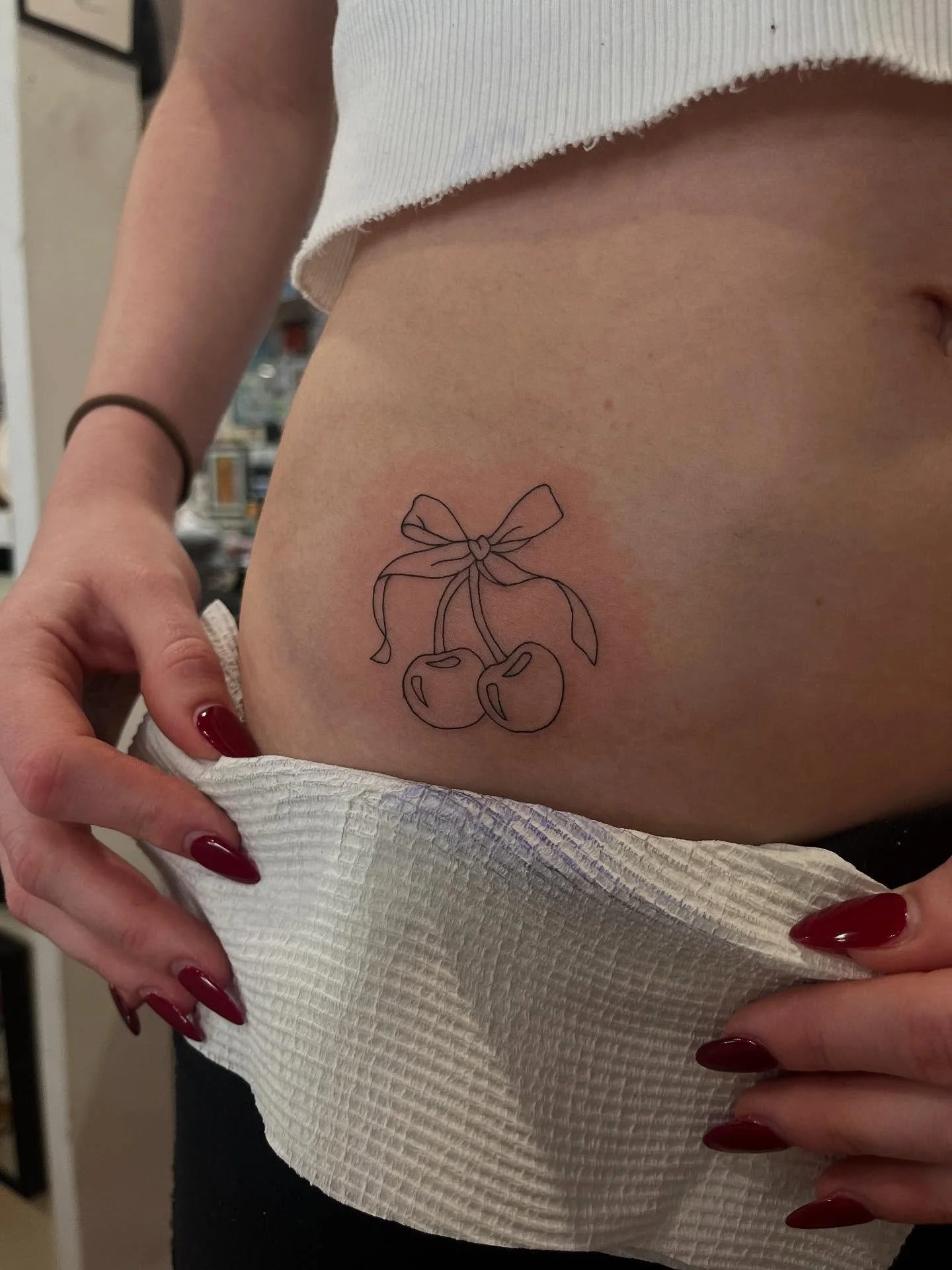 A tattoo of cherries with a bow on a person's lower abdomen.