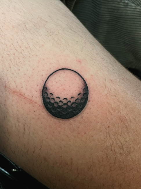 Tattoo of a golf ball on a person's arm.