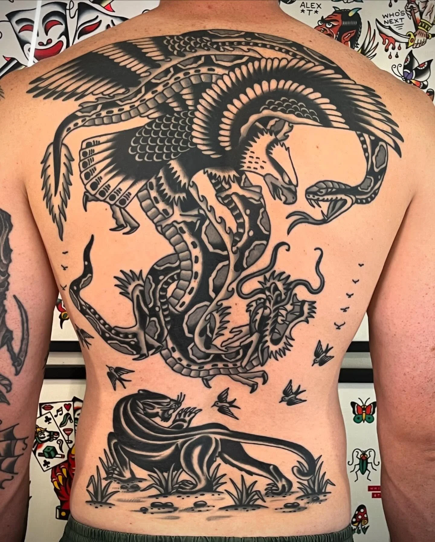 Black tattoo of a fierce dragon battling a bird, with trees and flying birds around them.
