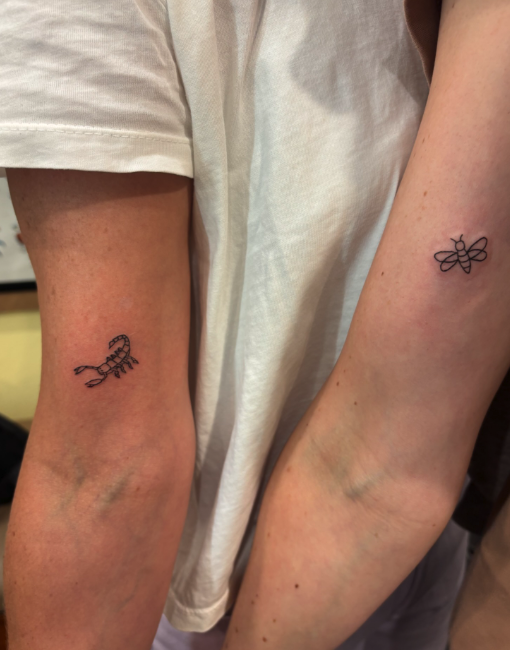 Two forearms with small black tattoos: one tattoo is a bee, and the other is a caterpillar.