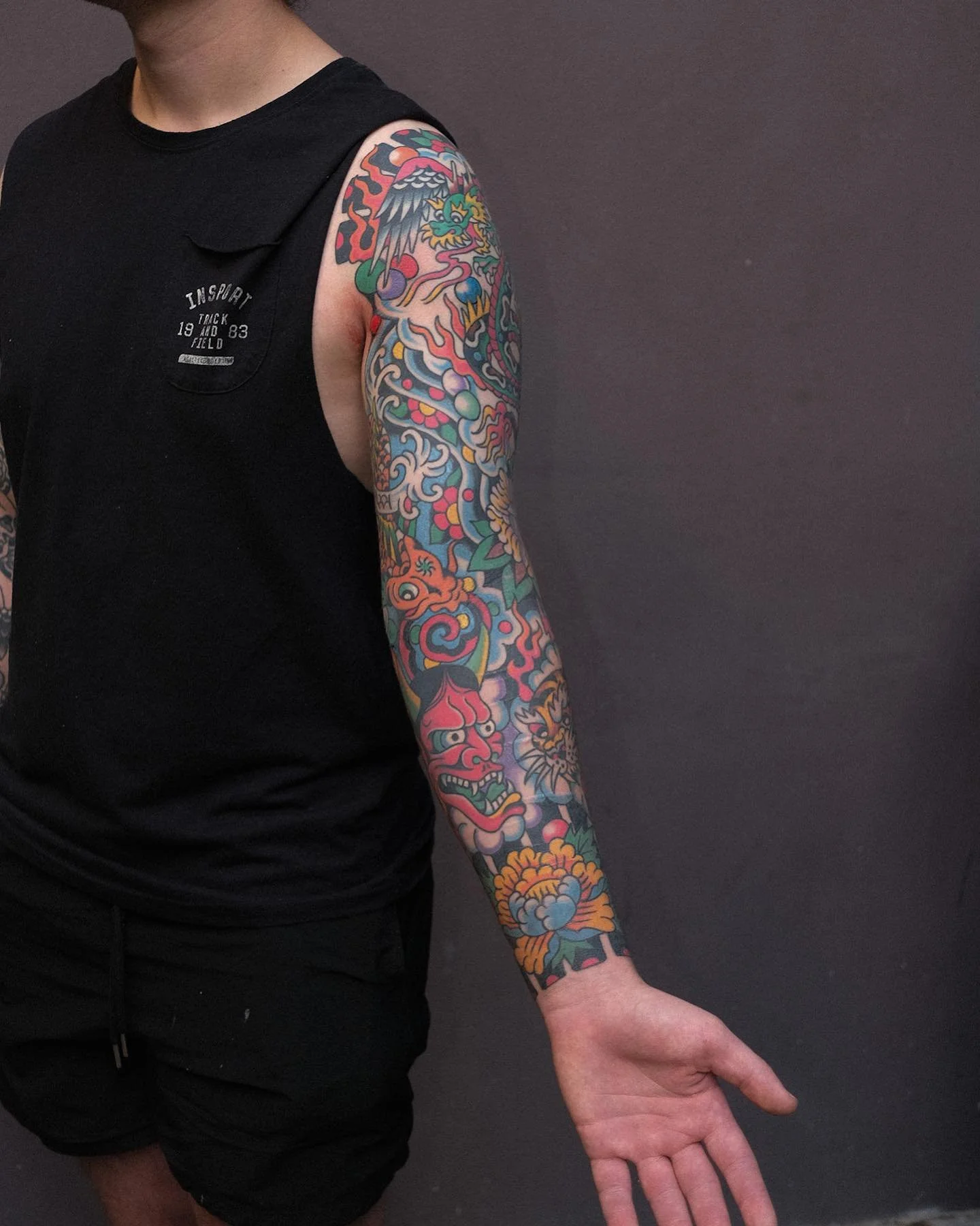 A person's arm with a colorful traditional-style Japanese tattoo featuring a dragon, lion, and floral designs.