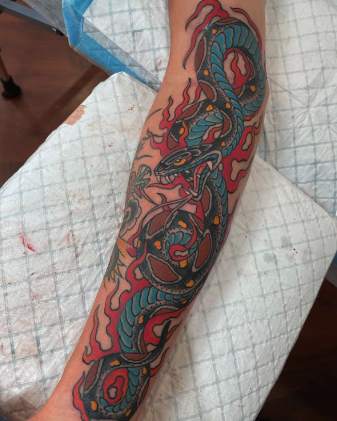 Colorful tattoo of a snake on a person's arm, with fiery red flames in the background.