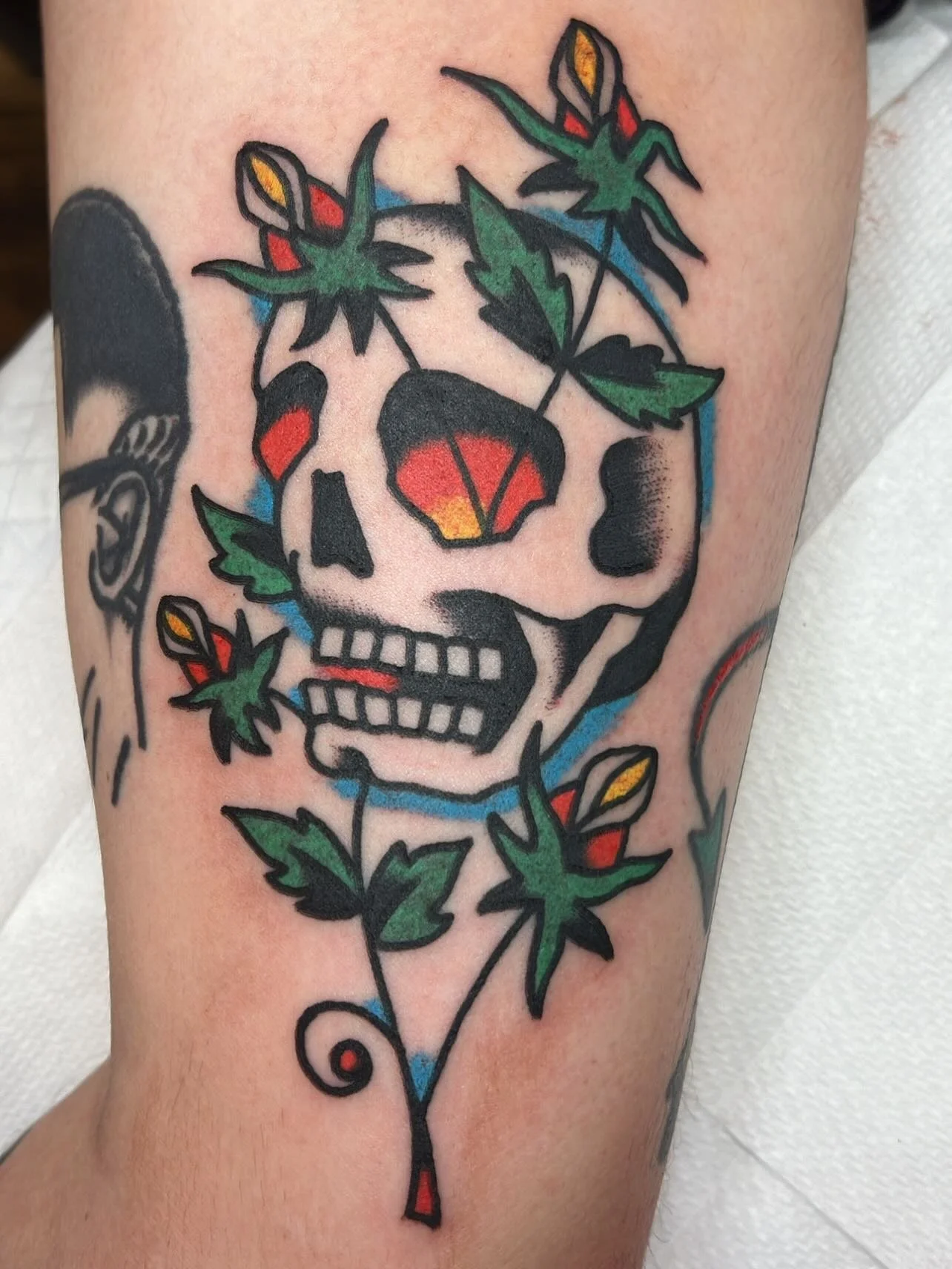 Tattoo of a skull with colorful leaves and flowers surrounding and intertwined with it.