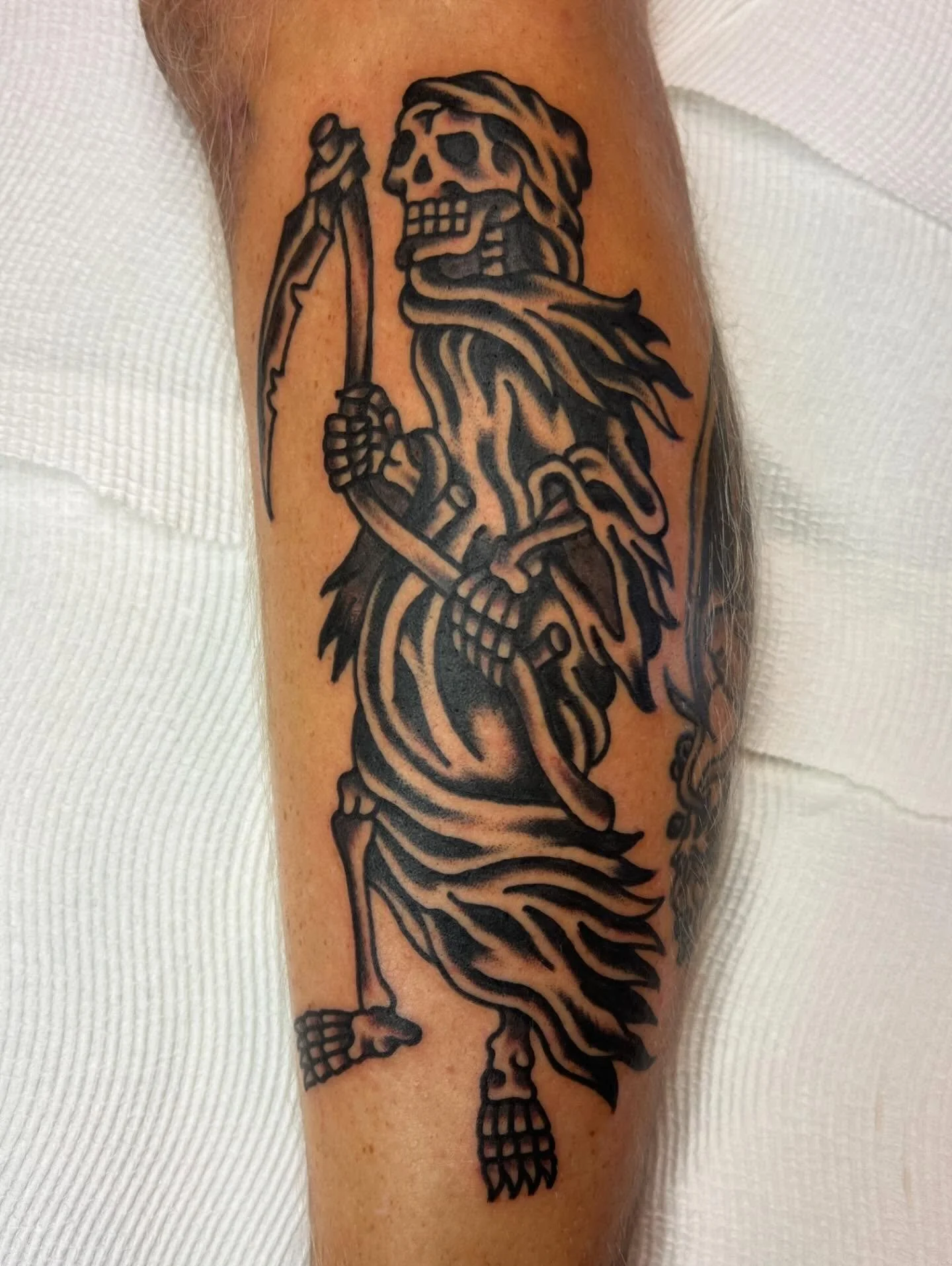 Black tattoo of a skeleton lion holding a scythe on a person's arm.