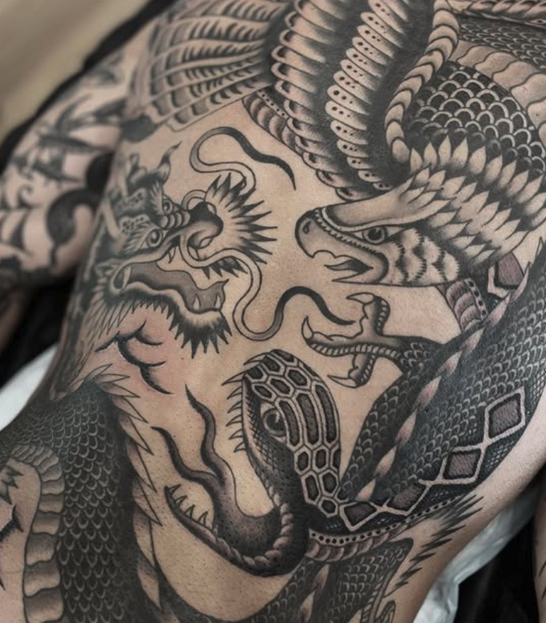 Black and gray Japanese-style dragon tattoo on person's upper body, featuring a fierce dragon with detailed scales and a snake-like body.