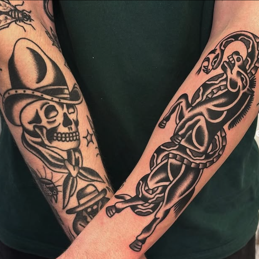 Tattoo of a skeleton cowboy with a hat, bolo tie, and a star on his chest on the left arm; tattoo of a rearing horse with a saddle on the right arm.