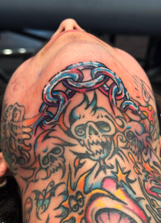 Colorful tattoo featuring a skull with fire, lightning, stars, and chains on a person's shoulder.