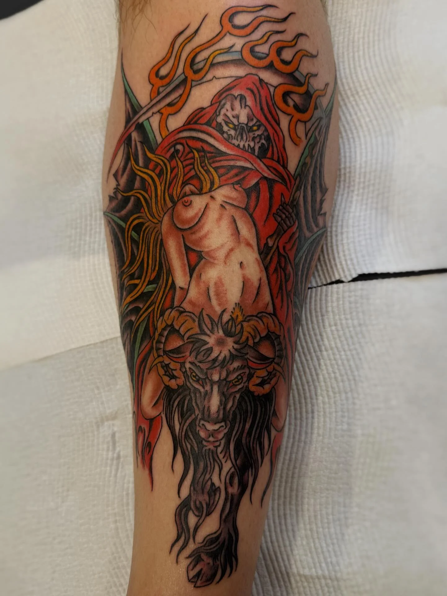 Tattoo of a lion with a mane that transforms into flames, a nude woman with long hair, and a grim-faced robed figure with a sword in the background.