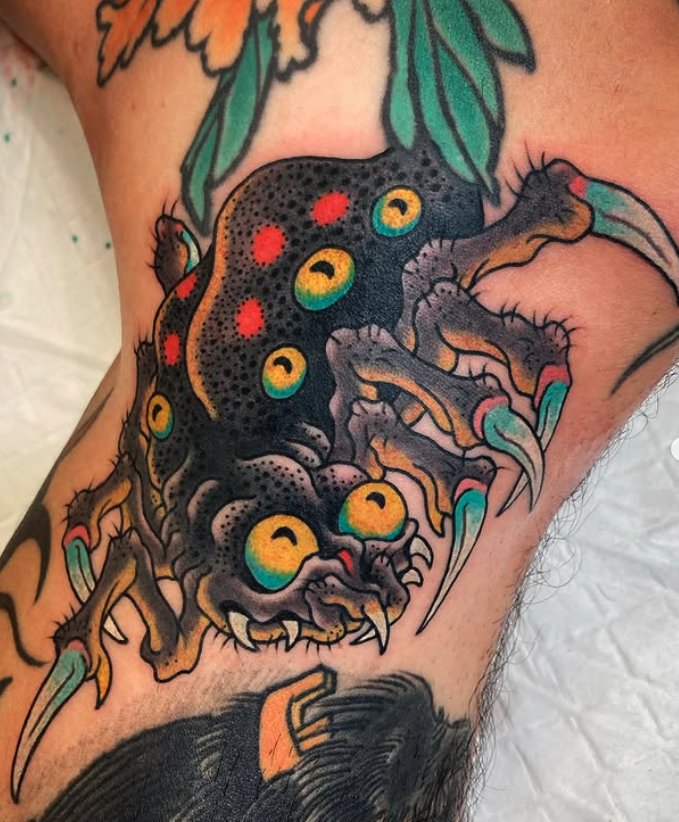 Colorful tattoo of a spider with multiple yellow and red eyes on a person's skin.