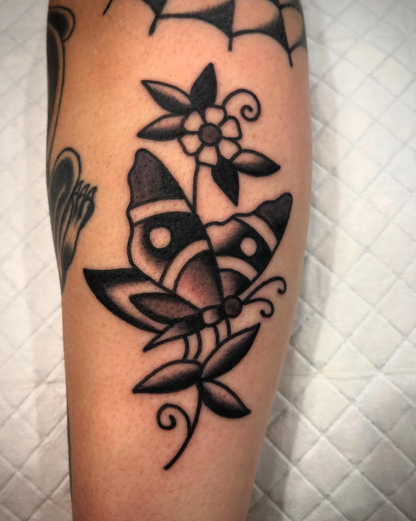 Black outline tattoo of a butterfly with floral and leaf design on skin.