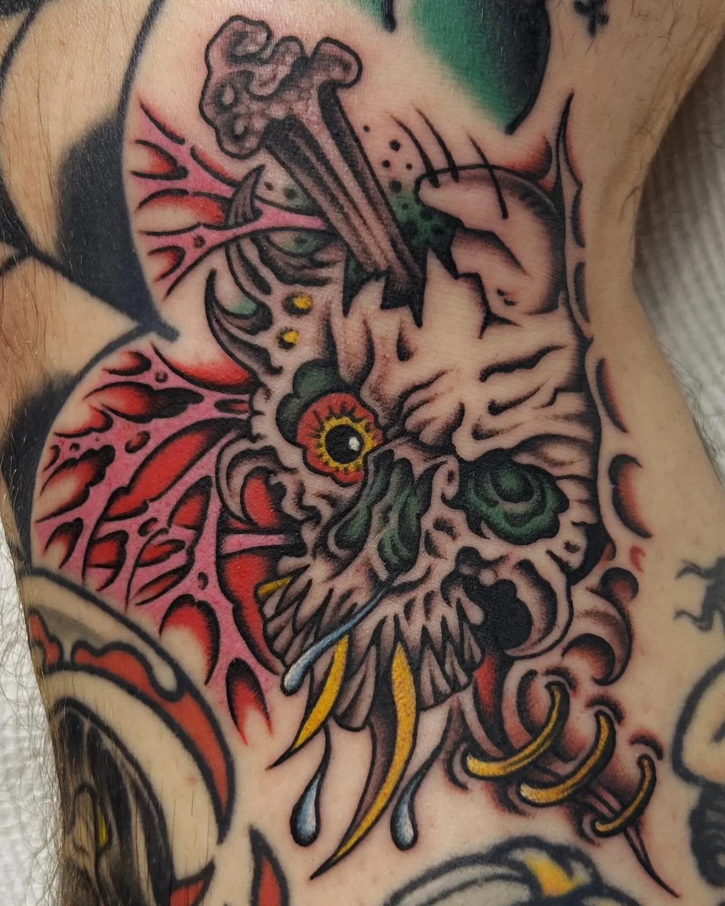 A colorful tattoo of a dragon's face with intricate details, surrounded by abstract patterns and vibrant shades of pink, red, green, yellow, and black.