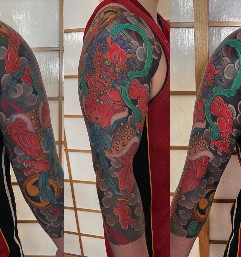 Close-up of a person's arm tattoo featuring a fierce red tiger with green eyes, surrounded by clouds and traditional Japanese elements.