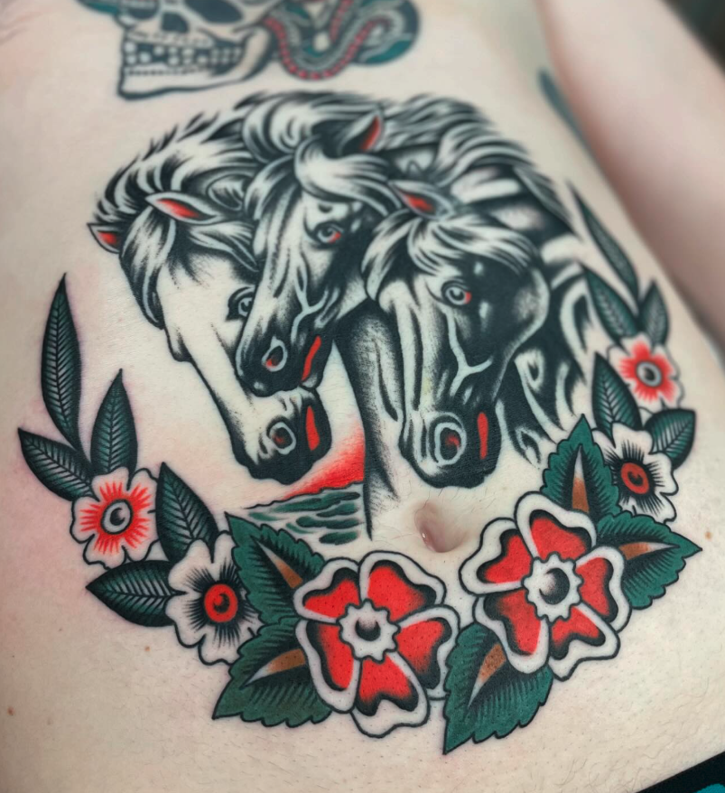 Tattoo of three black and white horses heads with red accents, surrounded by red, white, and green flowers and leaves.