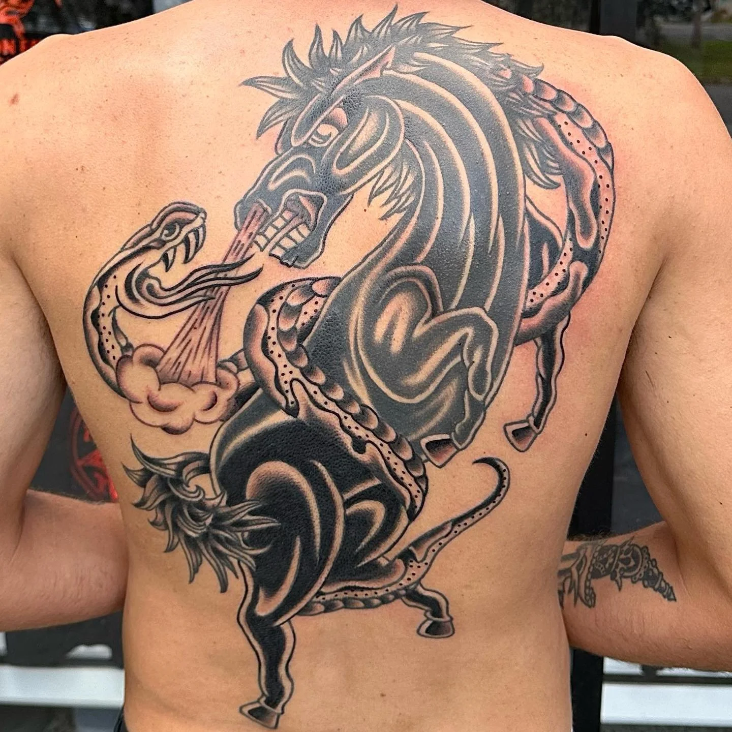 Black and gray tattoo of a fierce, mythical horse with sharp features, flames, and smoke elements on a person's chest.