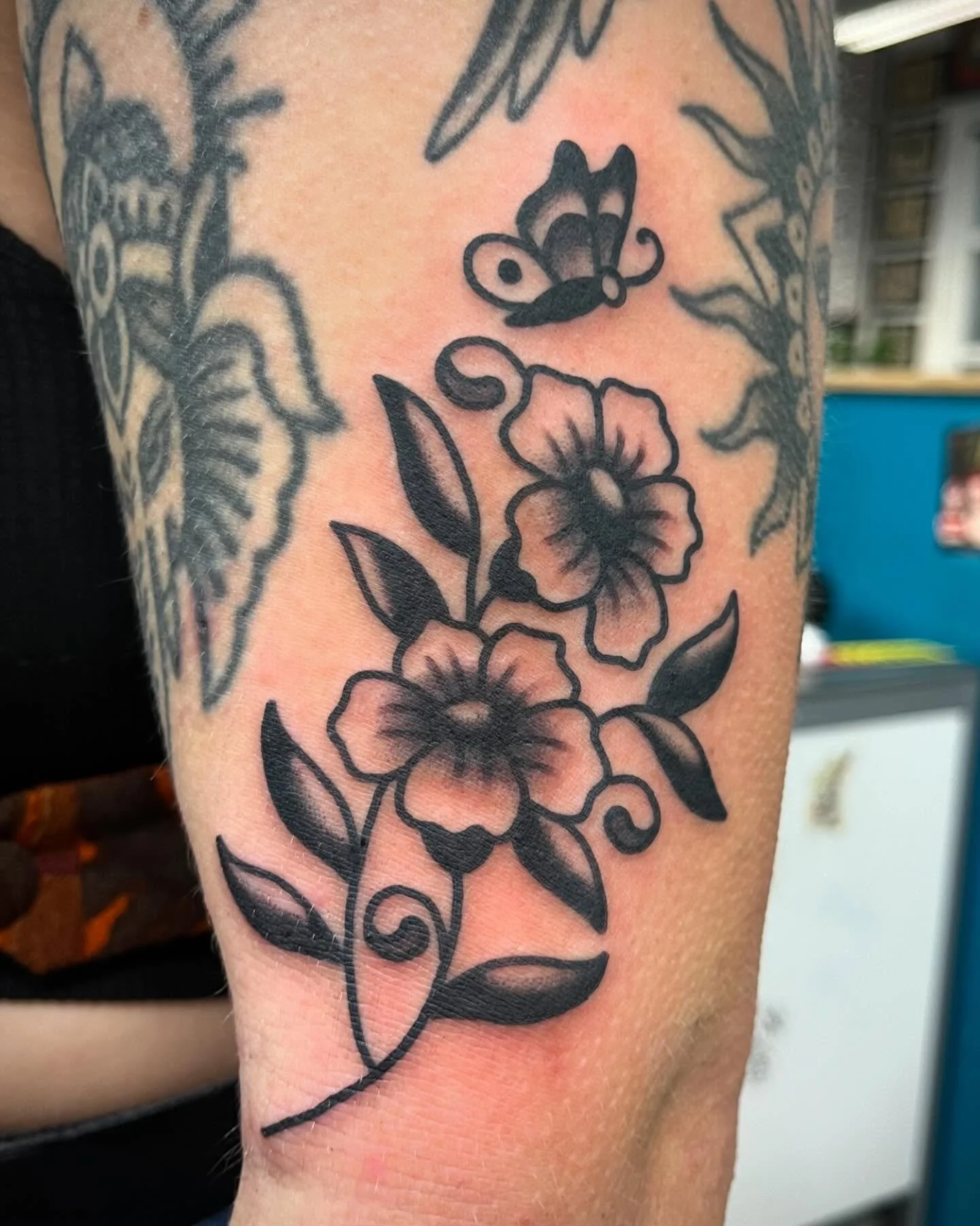 Black ink tattoo of two flowers with leaves and a bee flying above