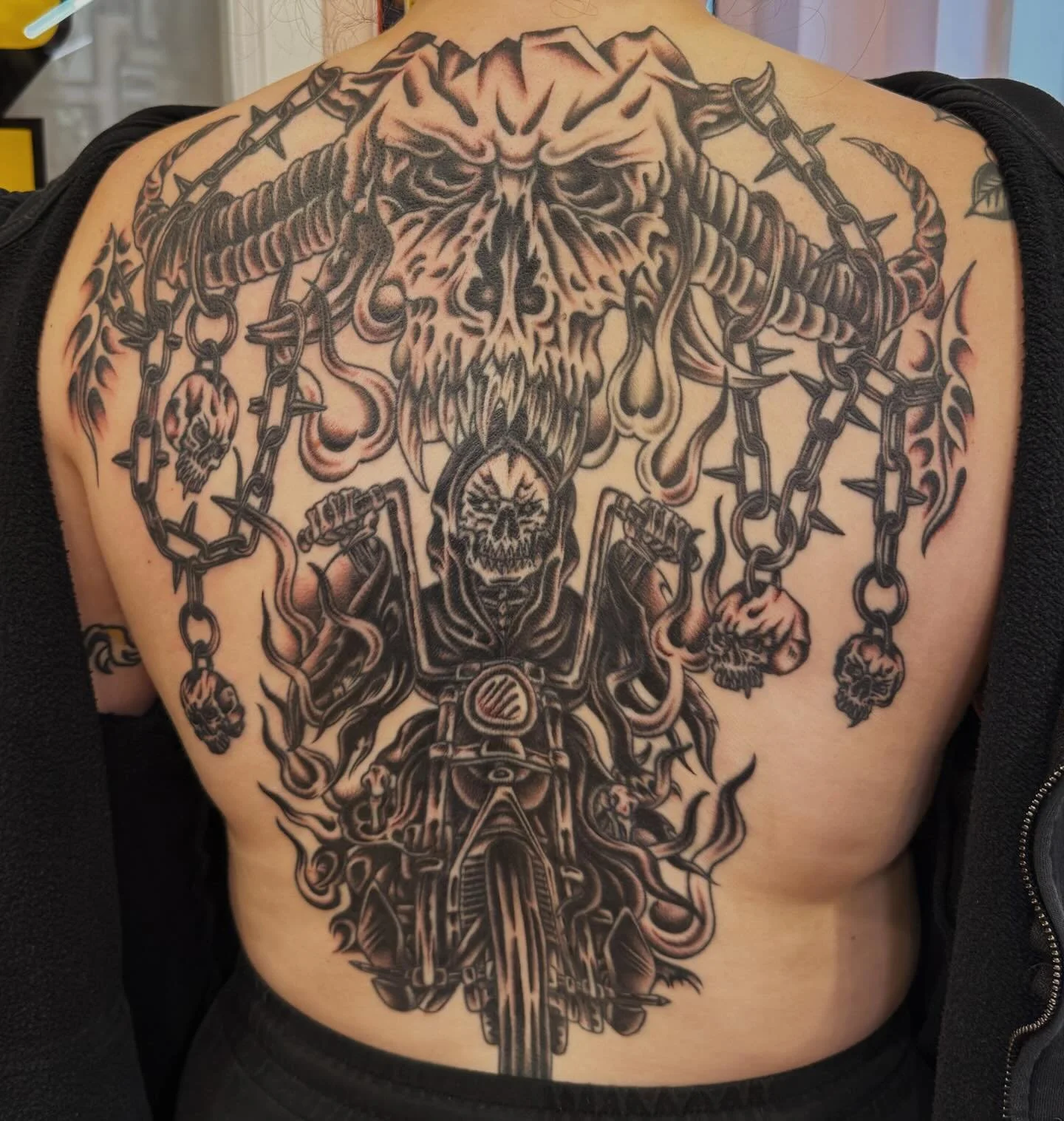Back tattoo of a skull with chains, a motorcycle, and flames.