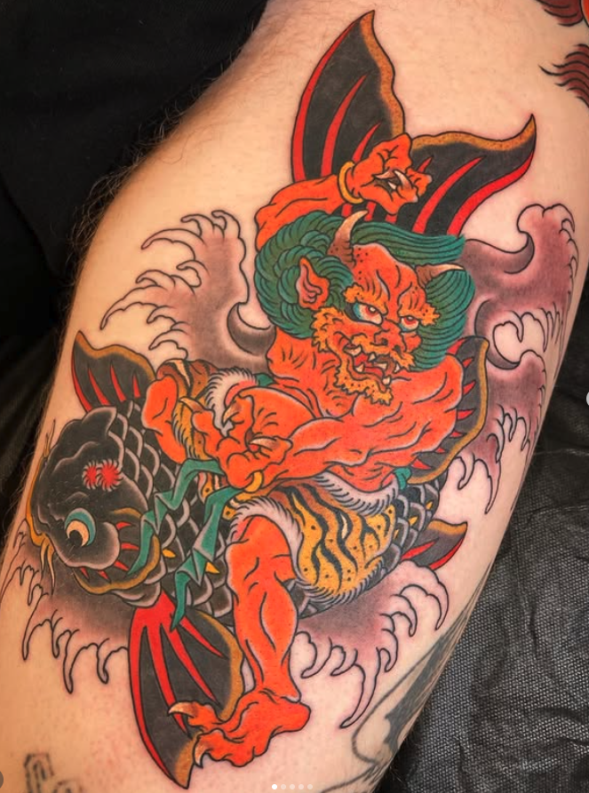 Tattoo of a fierce, orange tiger-like creature with green hair, holding a black fish with red eyes, amidst stylized clouds.