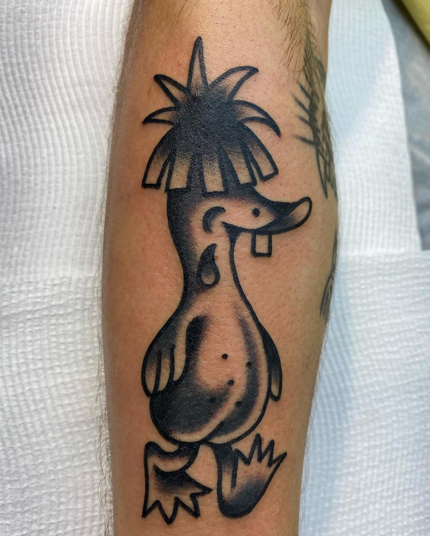 Tattoo of a cartoon-style mermaid with spiky hair, a prominent nose, and a playful expression, depicted in black ink.
