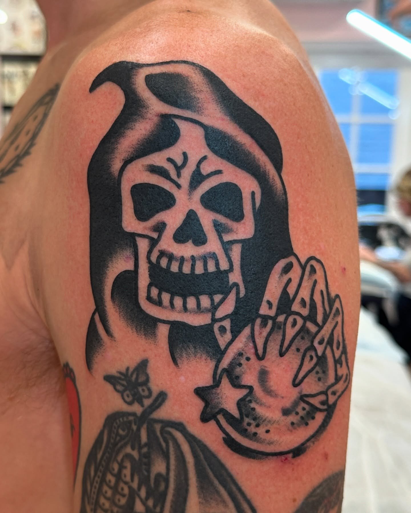 Tattoo of a skull with a hood and a skeleton hand, with a small butterfly and star nearby.