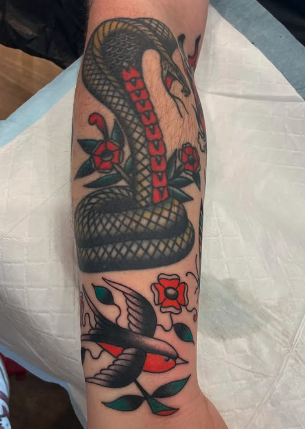 Tattoo of a yellow and black snake wrapped around a branch with red flowers and green leaves, and a traditional style swallow tattoo with a red circle background.