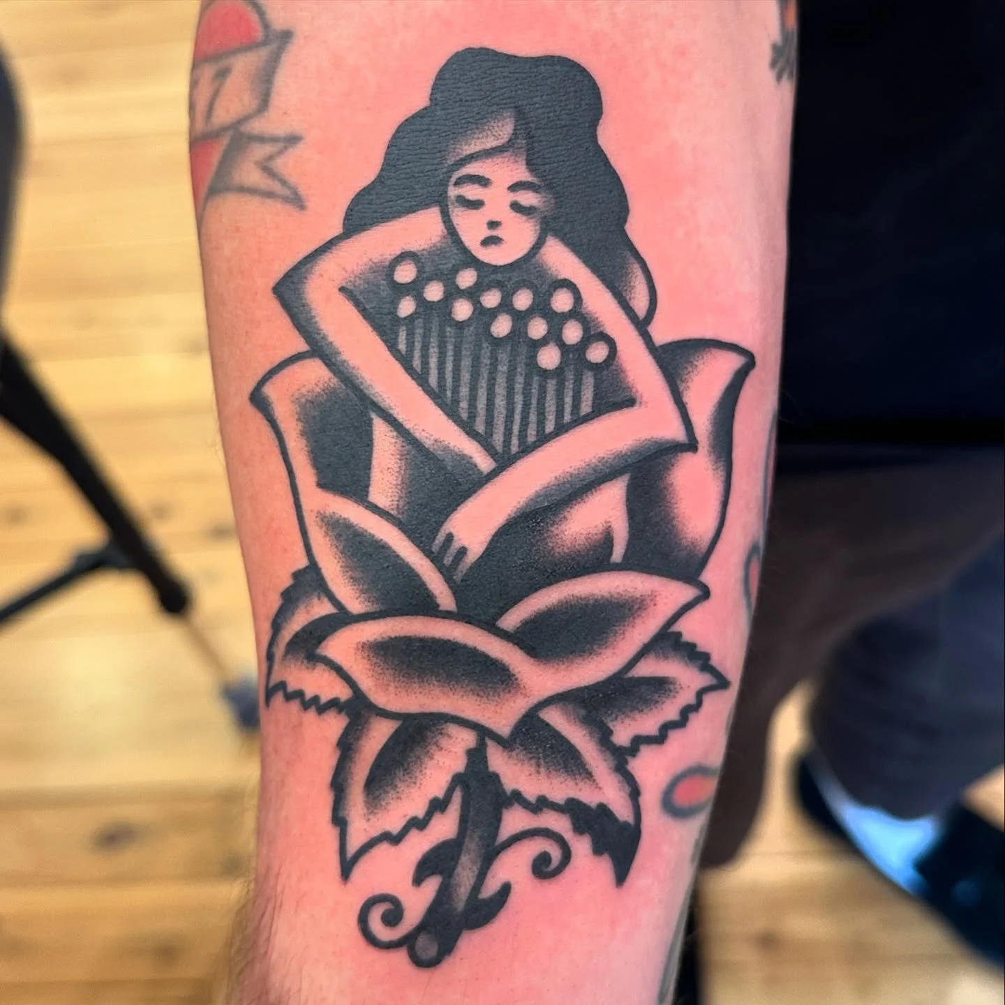 Tattoo of a woman with dark hair, sitting with her arms crossed, inside a blooming rose.