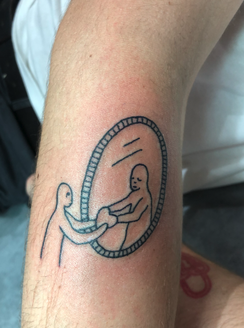 Tattoo of a mother holding her baby in front of an oval mirror on person's arm.