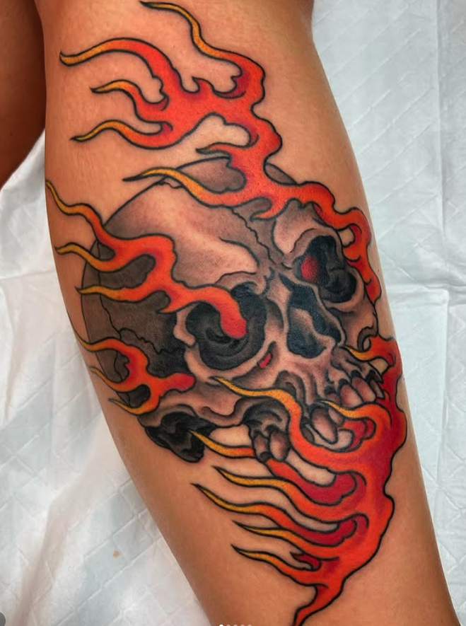 Tattoo of a realistic skull surrounded by flames on a person's thigh.