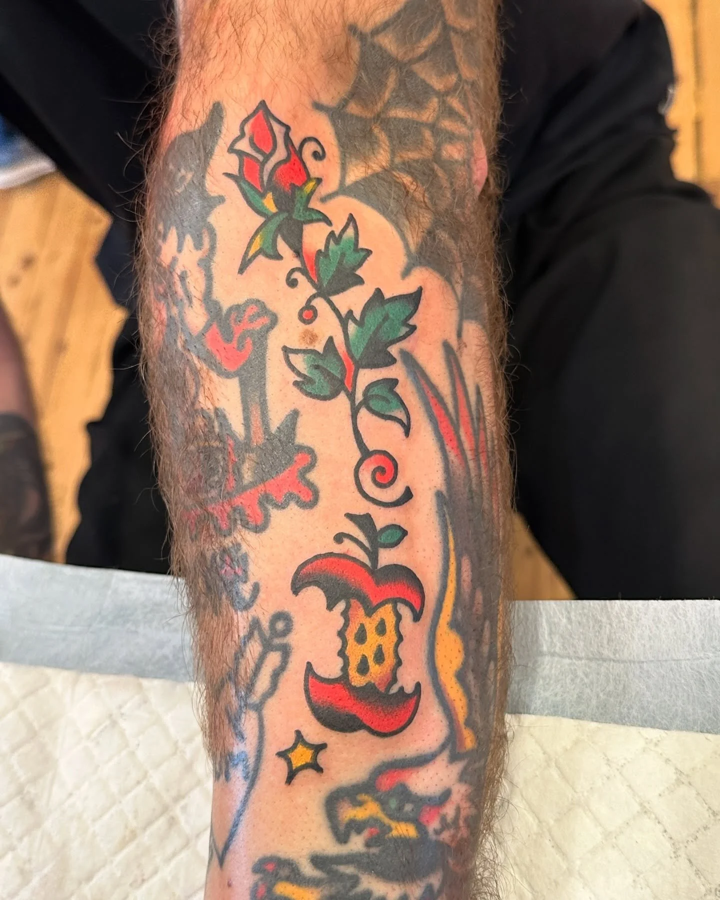 A tattoo on a person's arm featuring a red and green rose, a yellow and red bee, and various abstract and floral designs.