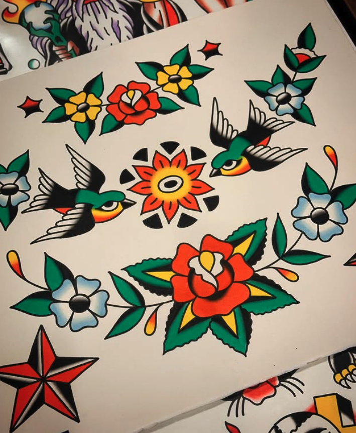 Colorful traditional tattoo-style design featuring flowers, two hummingbirds, and a central sun-like motif on white paper.
