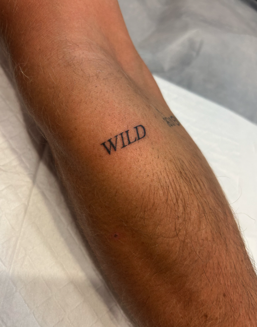 Close-up of a person's forearm with a tattoo reading 'WILD' and part of another word visible.