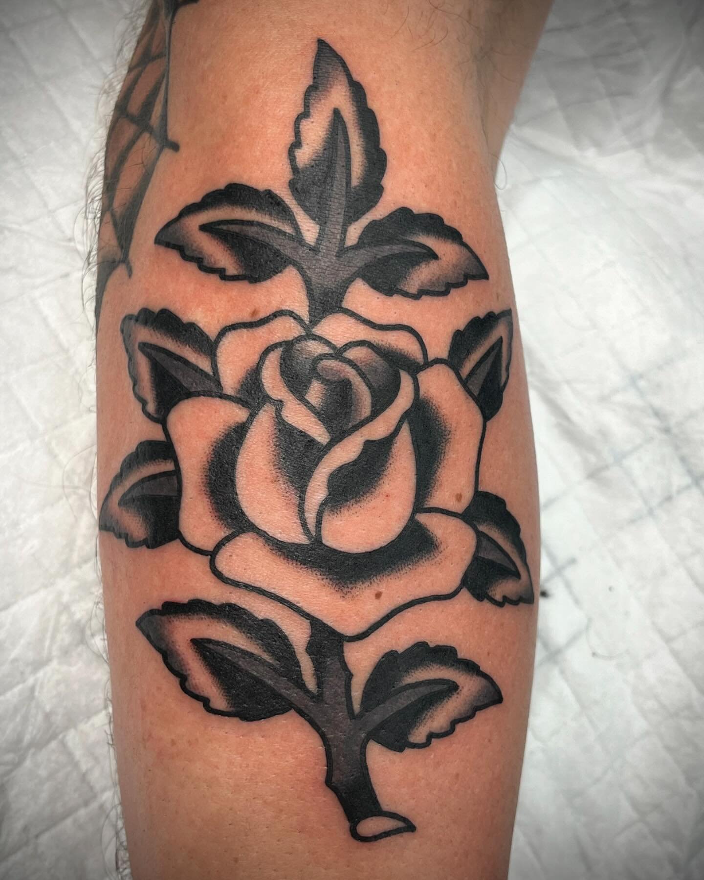 Black and gray tattoo of a rose with leaves on a person's arm.