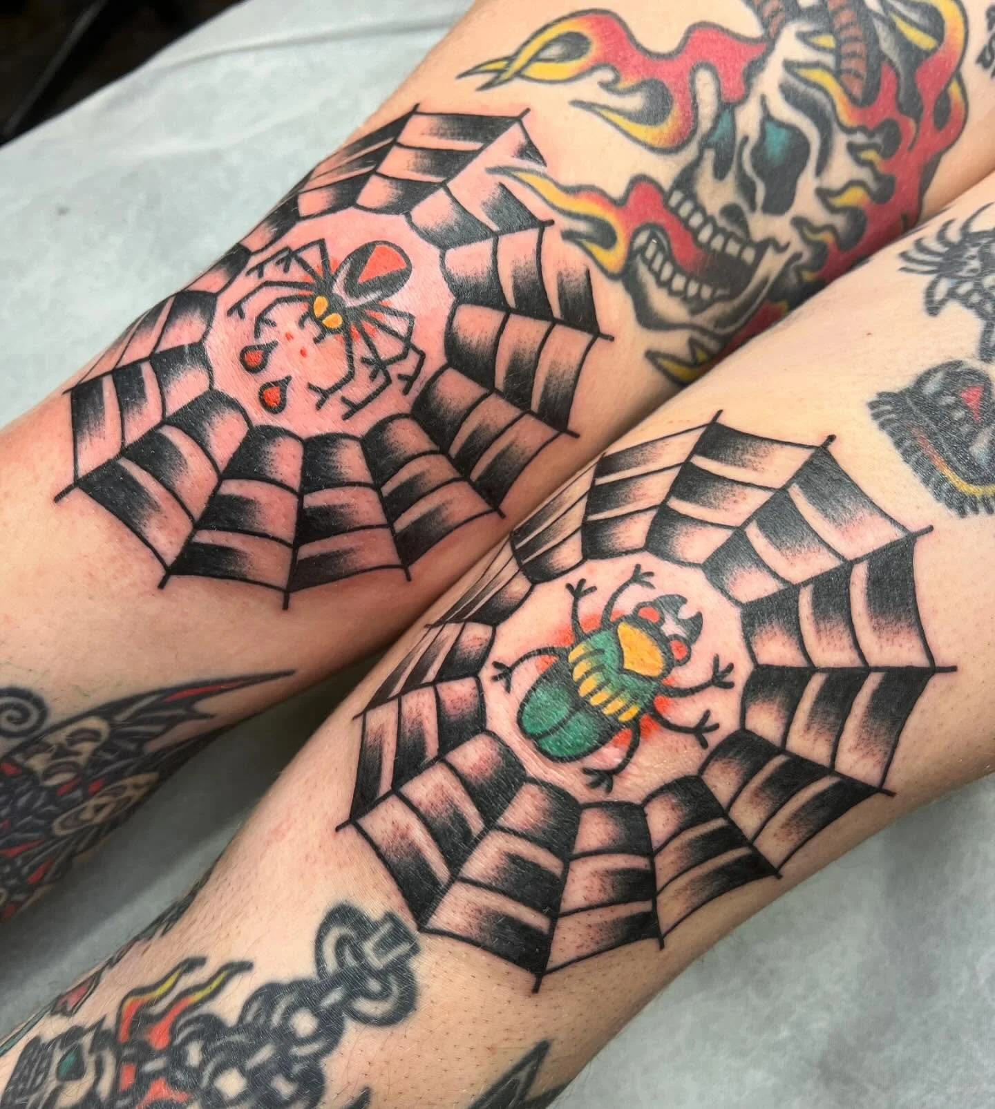 Tattoo of a spider and a beetle in their webs on the forearms of two people.