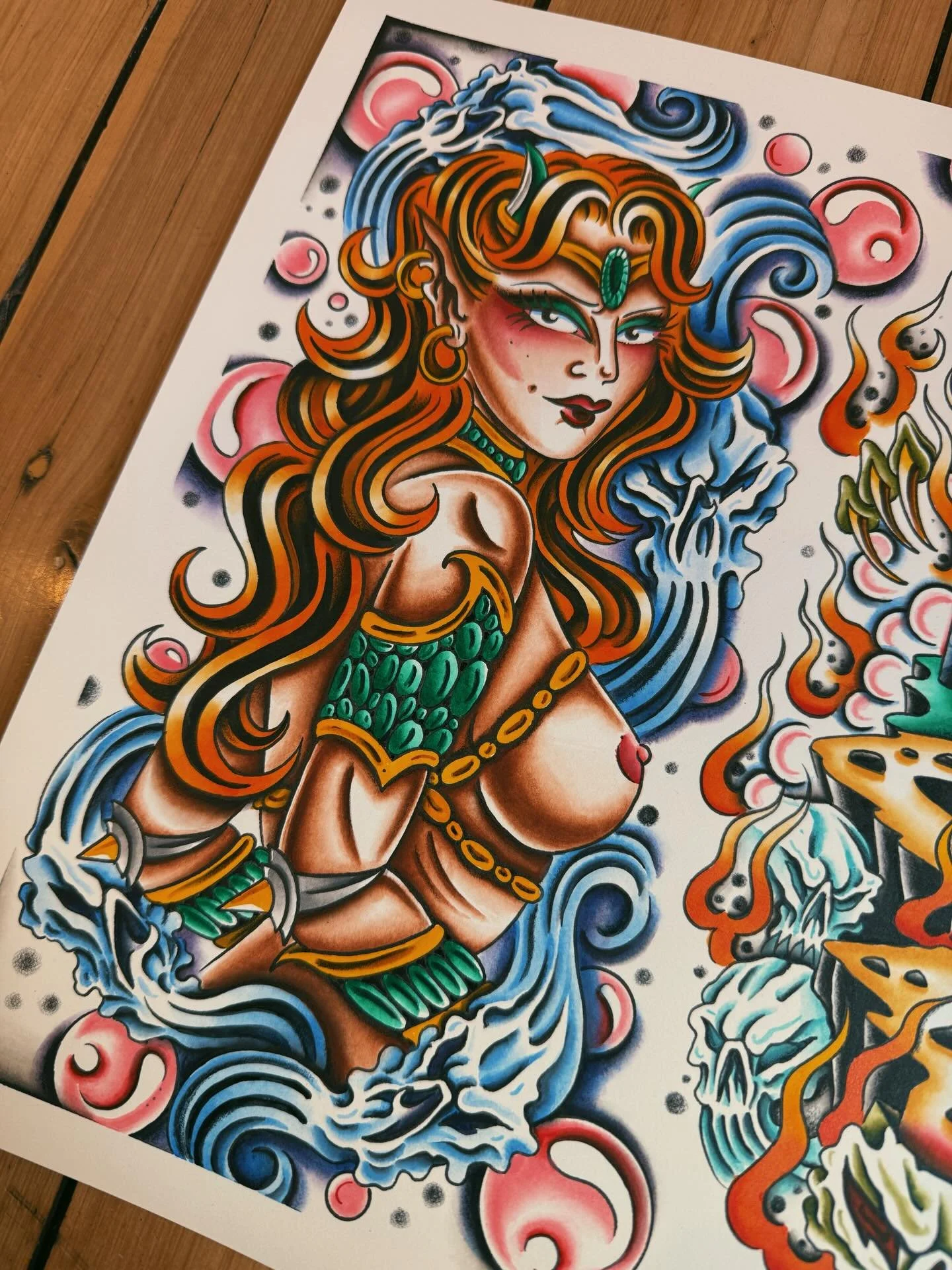 Colorful tattoo-style artwork of a fierce woman with long flowing orange hair, green jewelry, and a headpiece, surrounded by waves, clouds, and skulls.