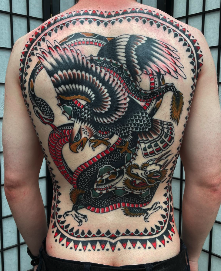 Large traditional Japanese style tattoo of a black and white dragon intertwined with a pheasant bird, surrounded by a decorative border, covering the person's back.