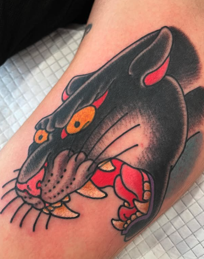 A colorful tattoo of a snarling panther on a person's arm, featuring black, red, yellow, and purple colors.